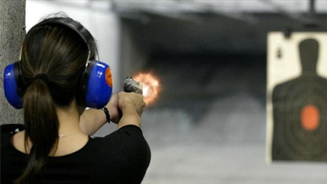 Image of back of a female shooting handgun in an indoor range